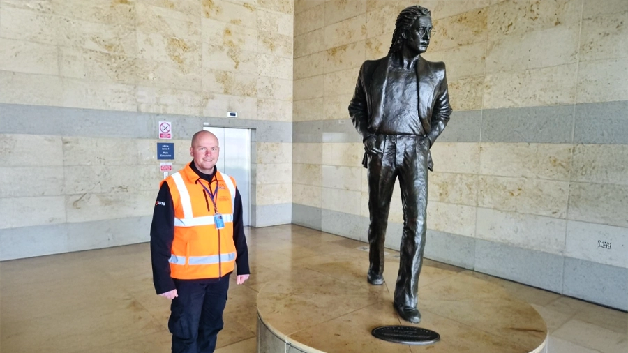 Geoffrey Swales standing next to the John Lennon statue inside Liverpool John Lennon Airport terminal